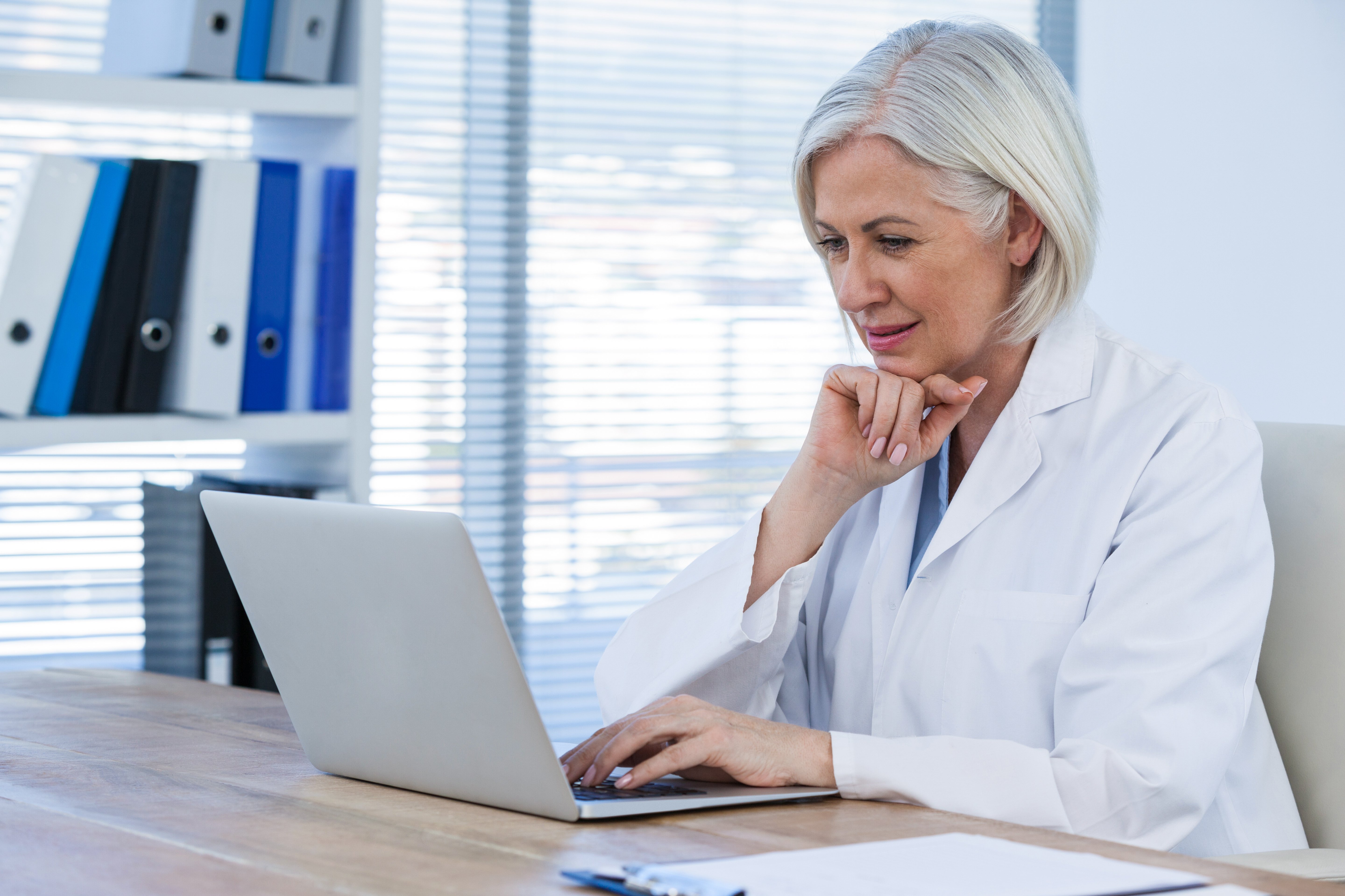female-european-elderly-doctor-consultation-room-working-on-her-laptop-print